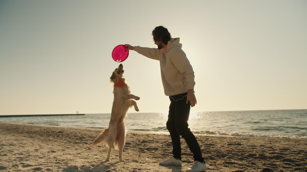E un giovane, insieme al suo grande cane dal pelo chiaro, giocano sulla spiaggia al mattino