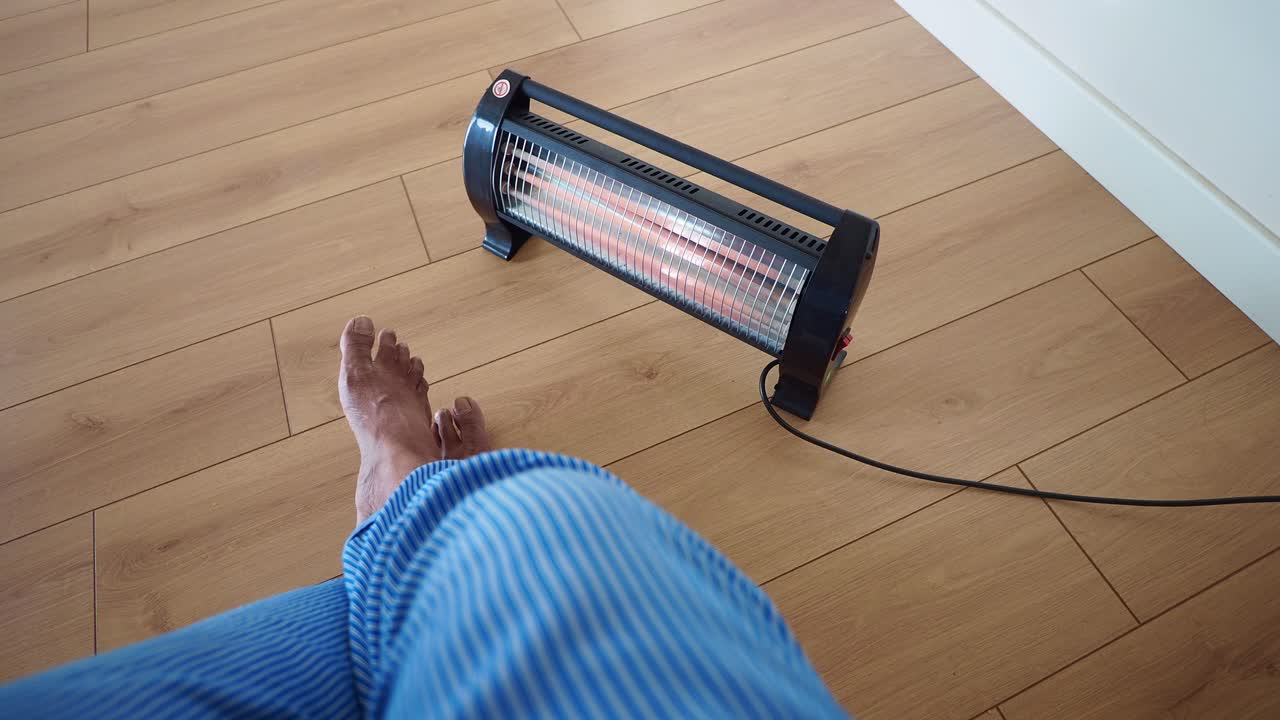 Person warming feet with infrared heater on wooden floor