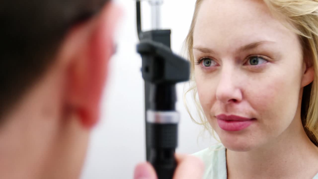 Optometrist examining female patient through ophthalmoscope