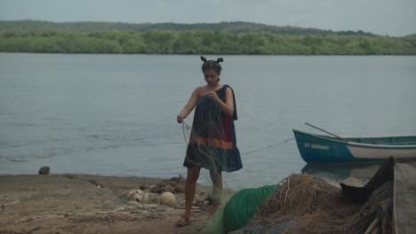 a young girl dressed in a navy elegant dress stands by the edge of a water reservoir, holding fishing nets in her hand