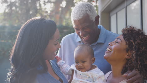 grandparents with adult daughter and baby granddaughter playing in garden at home together