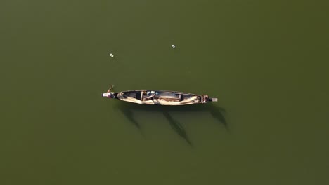 top down aerial shot of a small wooden boat in a lake and fishermen catching fish with net in traditional style
