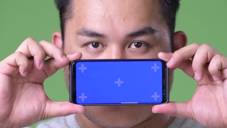 young handsome overweight asian man against green background