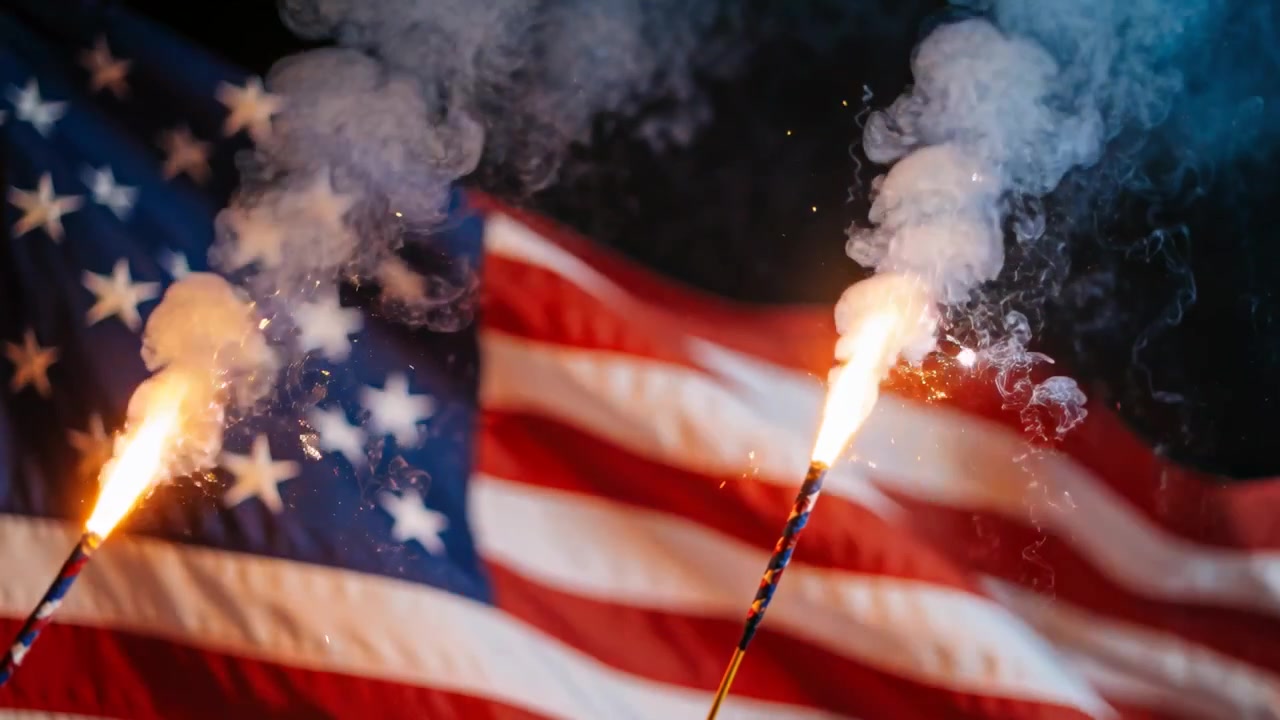 Igniting two handheld sparklers emitting bright sparks and rising smoke in front of American flag
