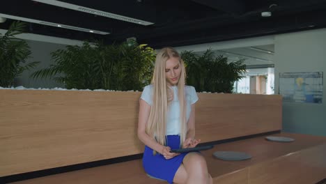relaxing woman with tablet in office. young elegant woman sitting barefoot on wooden tribune in modern office using tablet and taking rest
