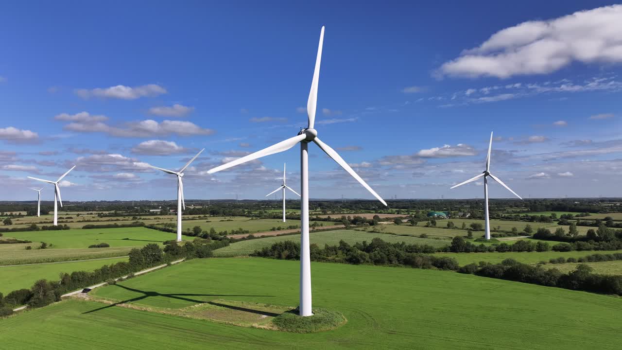 Wind turbines farming wind energy, green fields, blue sky, countryside, sunny, static drone shot, symbolic, picturesque