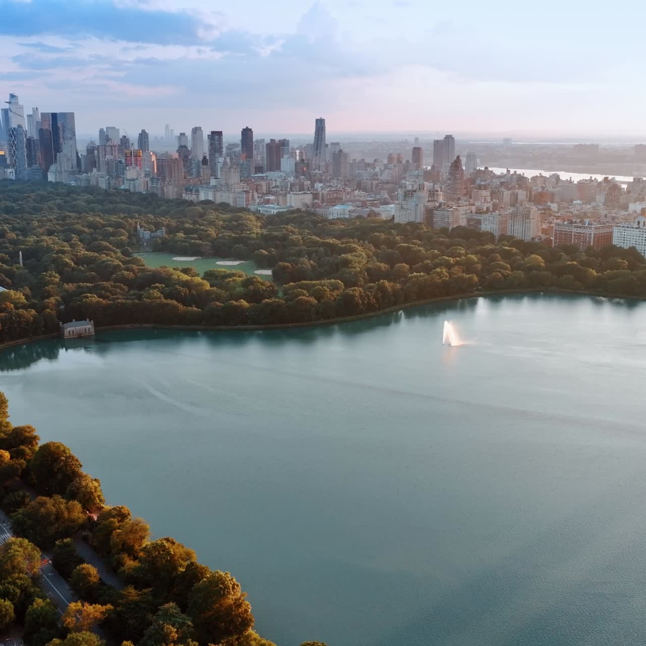View of marvelous New York skyscrapers from the side of Central Park. Drone footage above the Jaqueline Kennedy Onassis Reservoir at sunset