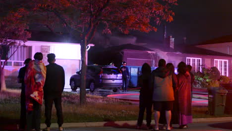 neighbors watch on as fire crews bring a house fire under control and continue to douse the roof with foam