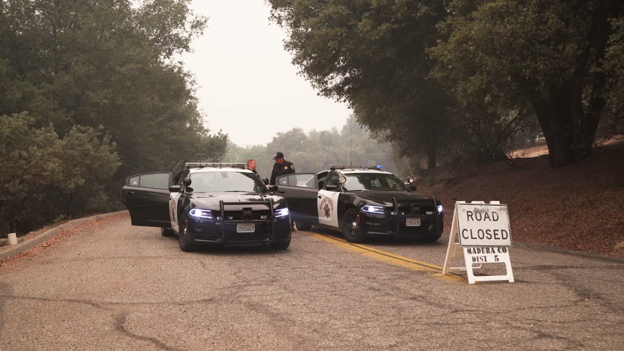 Police cars, lights flashing, block smoky road, Creek Fire, California