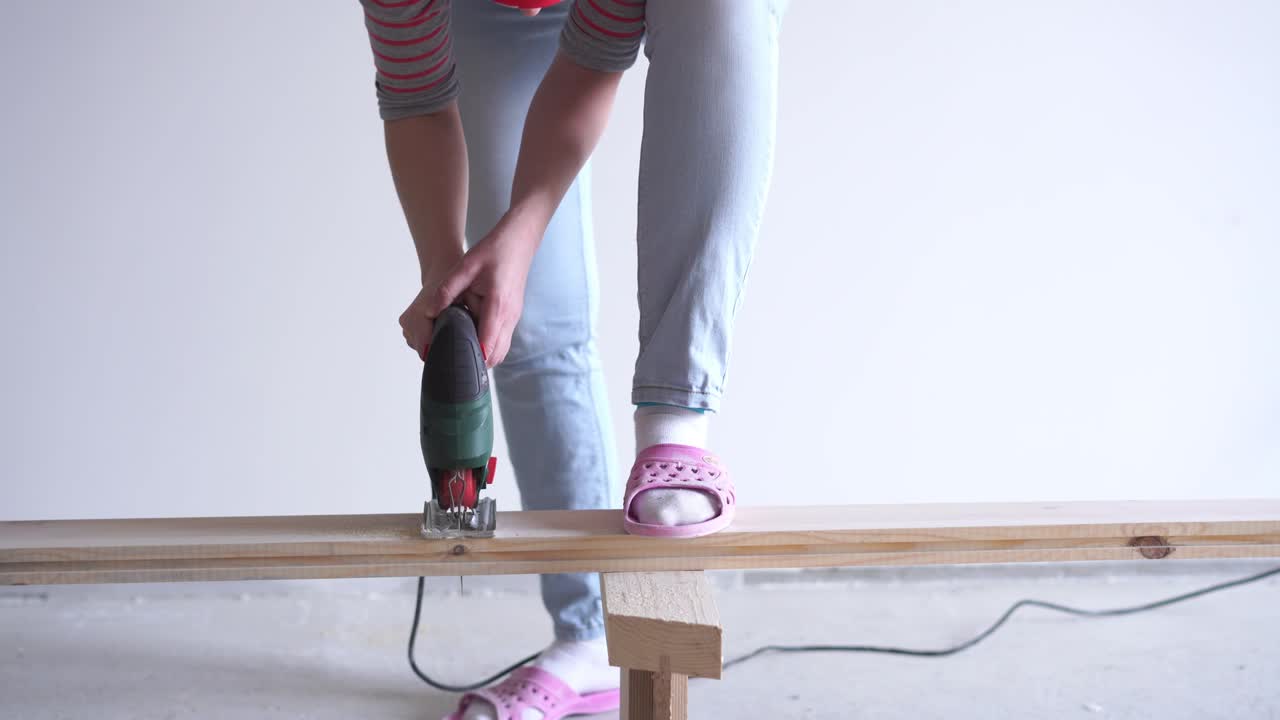 una mujer hace un trabajo no femenino - aserrar una tabla de madera con un rompecabezas eléctrico