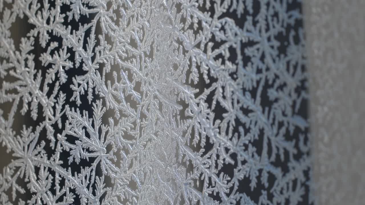 Close-up video of intricate frost patterns on glass, captured from a side angle