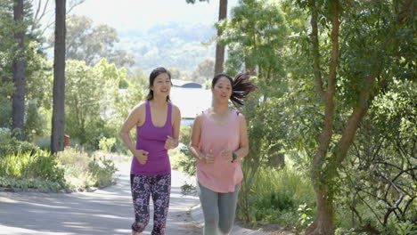 happy asian female friends running near forest on sunny day, slow motion