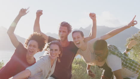 men lifting up women as group of friends have fun against flaring sun