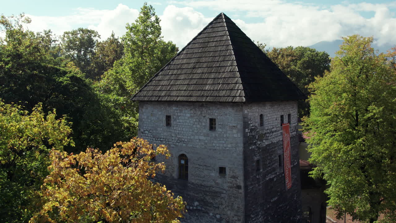 Aerial view of Kapetanova Kula, the historic medieval tower in Bihać, Bosnia and Herzegovina, surrounded by colorful autumn trees near the River Una under a bright blue sky