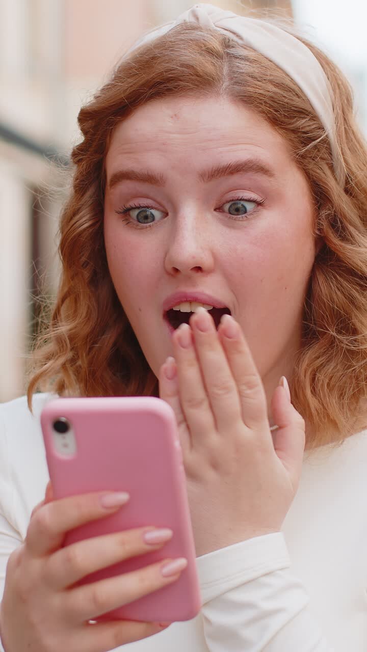 Eccitata felice vincitrice giovane donna usa lo smartphone per festeggiare la vittoria buone notizie per strada in città
