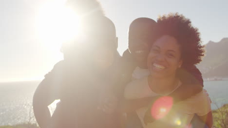 Portrait-Of-Parents-Giving-Children-Piggybacks-By-The-Sea