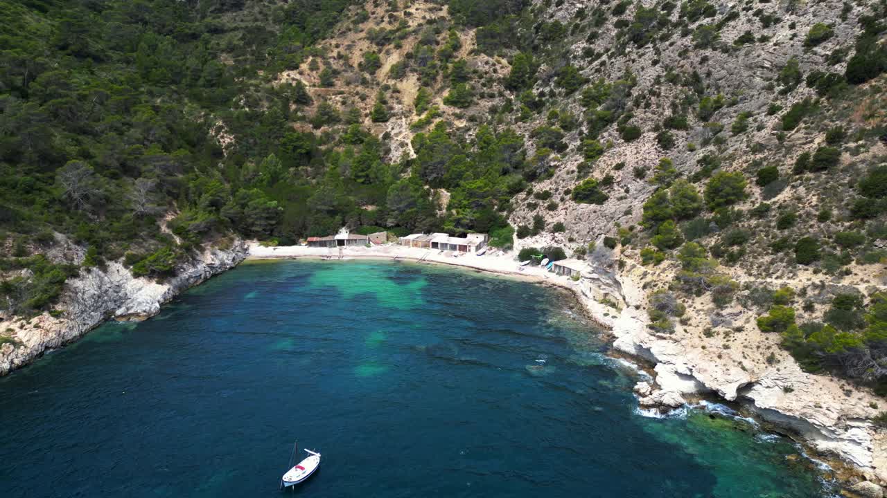 Cala Llentrisca beach with turquoise water and Barques de pescadors Huts in Ibiza, Spain, in summer. Dramatic aerial view flight circle drone footage