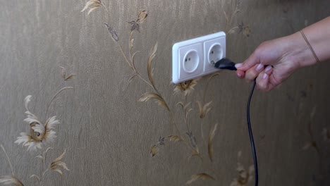 girl is unplugging a cord from the electricity socket to save energy as the prices raise