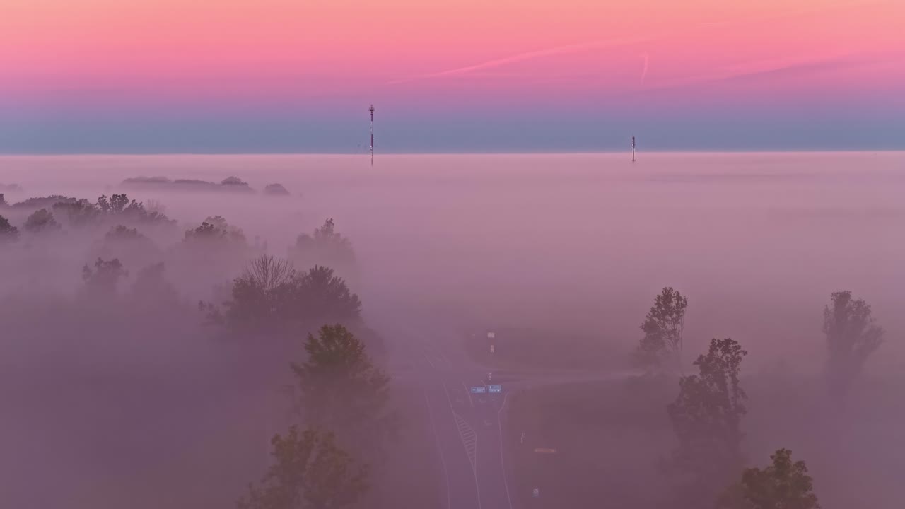 Aerial view over a pinkish mist hanging over the woods and a crossroads