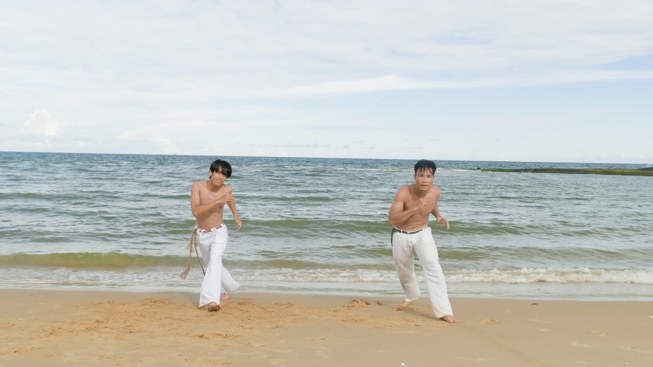 두 남자가 해변에서 카포에라를 춤추고 있다