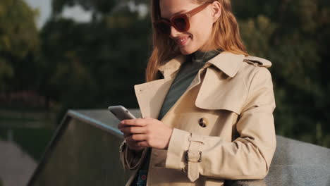 estudiante caucásica usando el teléfono inteligente y sonriendo al aire libre.