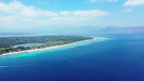 Peaceful-sea-scenery-of-blue-azure-lagoon-around-shore-of-tropical-island-with-boats-anchored-near-white-beach-on-bright-sky-with-white-clouds-in-Bali