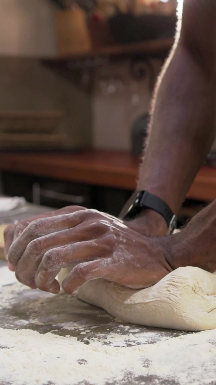 Vertical video: Kneading baker in apron shaping dough after being set on floured kitchen counter