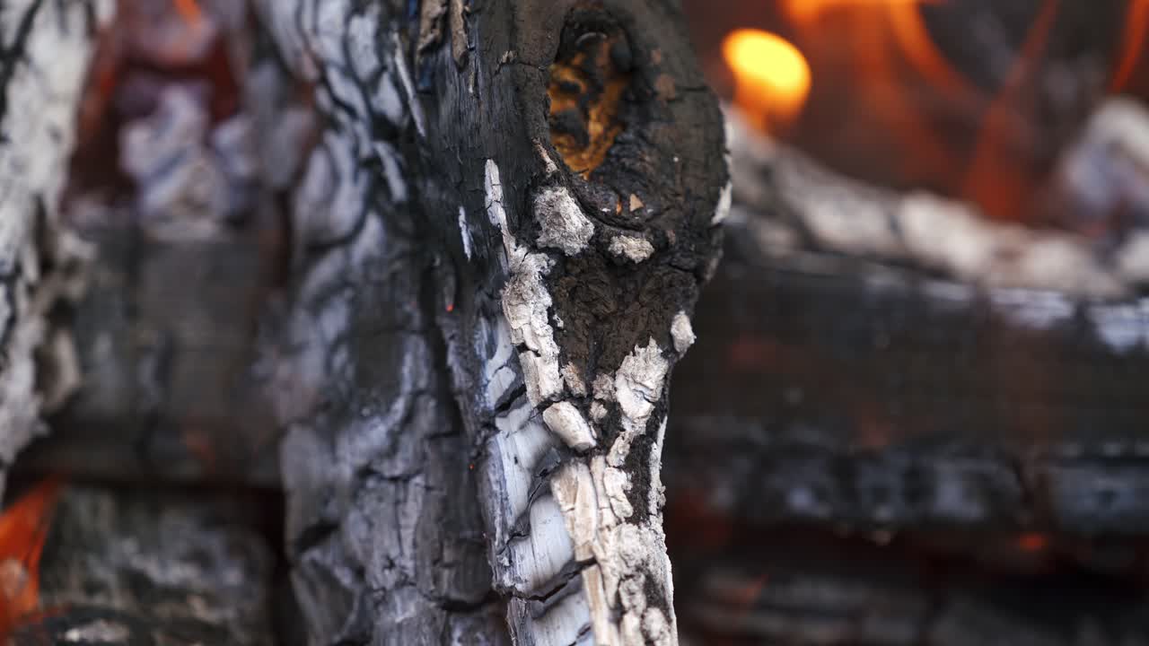 Embers in orange flame. Smoldering logs burning up in fire. Black smoldering wood with ash. Close-up.