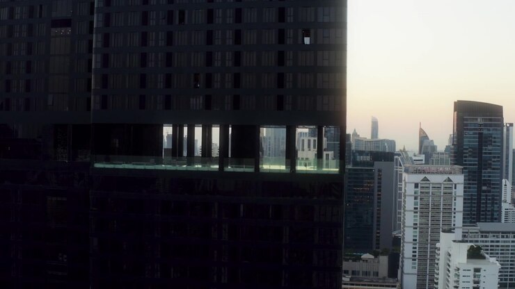 Dron panea a la derecha pasando una torre de cristal mientras el amanecer revela los tejados de Bangkok