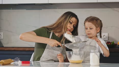 madre y hija tamizan la harina con tamiz en la mesa en la cocina