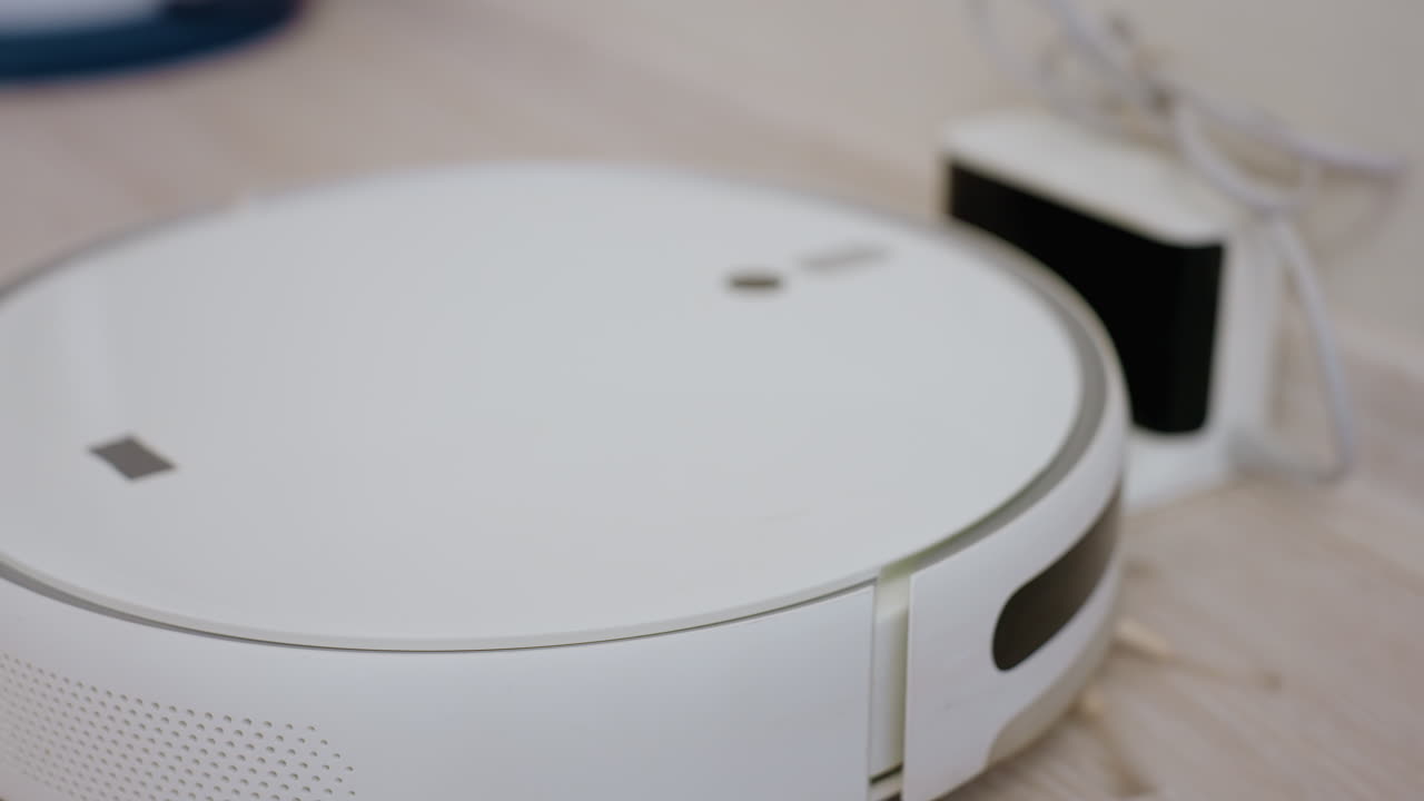 Close up robotic vacuum cleaner moving across wooden floor and stopping at charging station with glowing indicators, highlighting modern household cleaning technology
