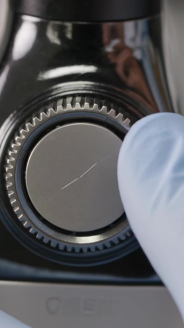 Vertical video: Approaching gloved finger probing hairline scratch on chrome dial at bench to check