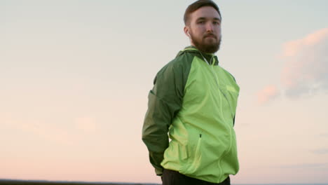 zoom in of young man in sportswear listening to music with headphones and looking at camera while standing outdoors in the morning