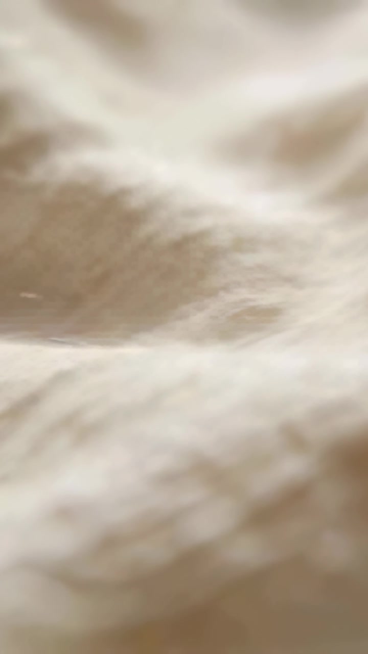 Vertikal video: Kamerafokus trækkes tilbage og afslører et nærbillede af beige tekstil, der udforsker vævning og fibre.