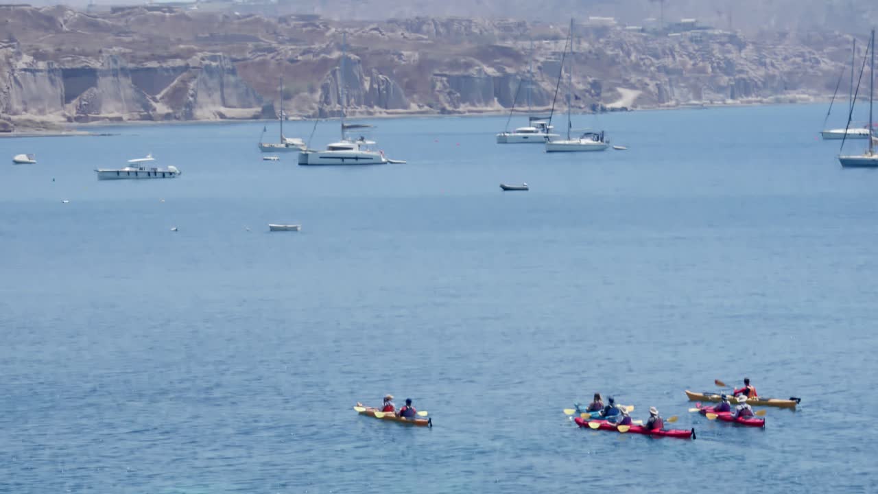 Group of people kayaking towards group of sailboats in Santorini, Greece
