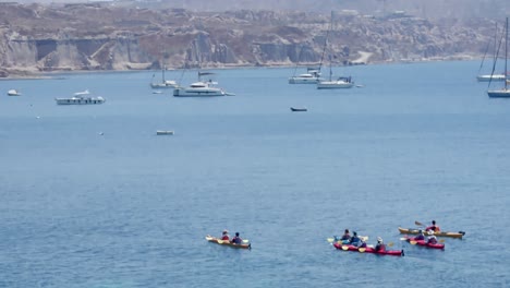 group of people kayaking towards group of sailboats in santorini, greece