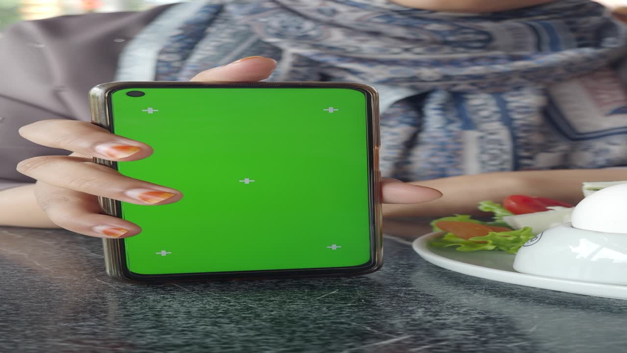 mujer con un teléfono inteligente de pantalla verde en un café