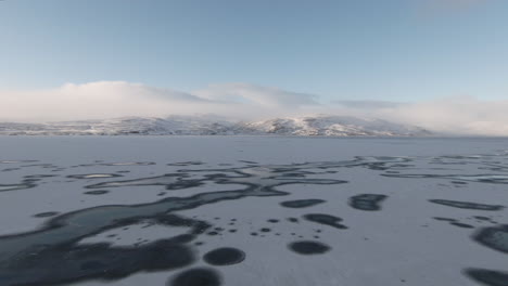 dolly forward above frozen lake towards towering, scenic mountains in background