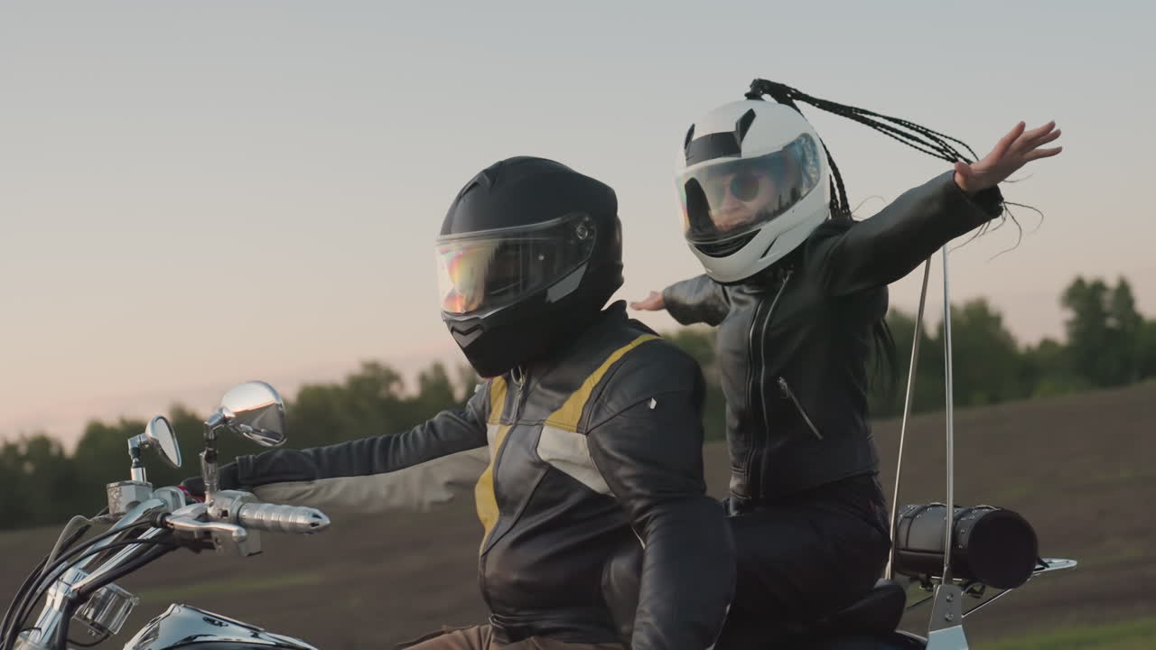 Traveler spreads hands wide while riding motorcycle with passenger on open highway at sunset, dramatic sky and road stretching ahead highlight freedom, adventure and lifestyle