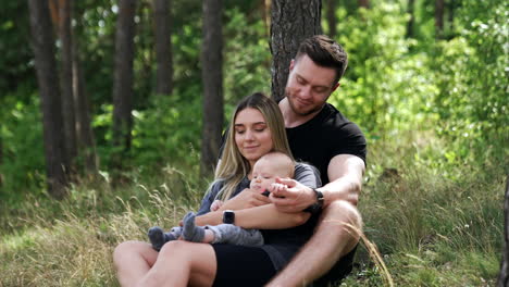 man and woman sit in the nature with their adorable newborn. caucasian family spending time in the forest.