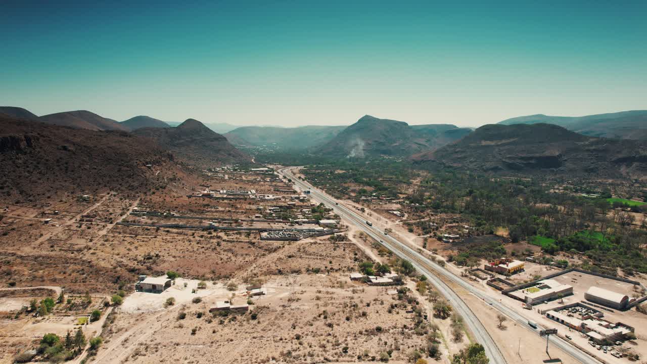 Aerial forward shot of a highway passing through a valley and from the center of a small town, countryside near Queretaro, Mexico - Sandia Mountains Albuquerque New Mexico