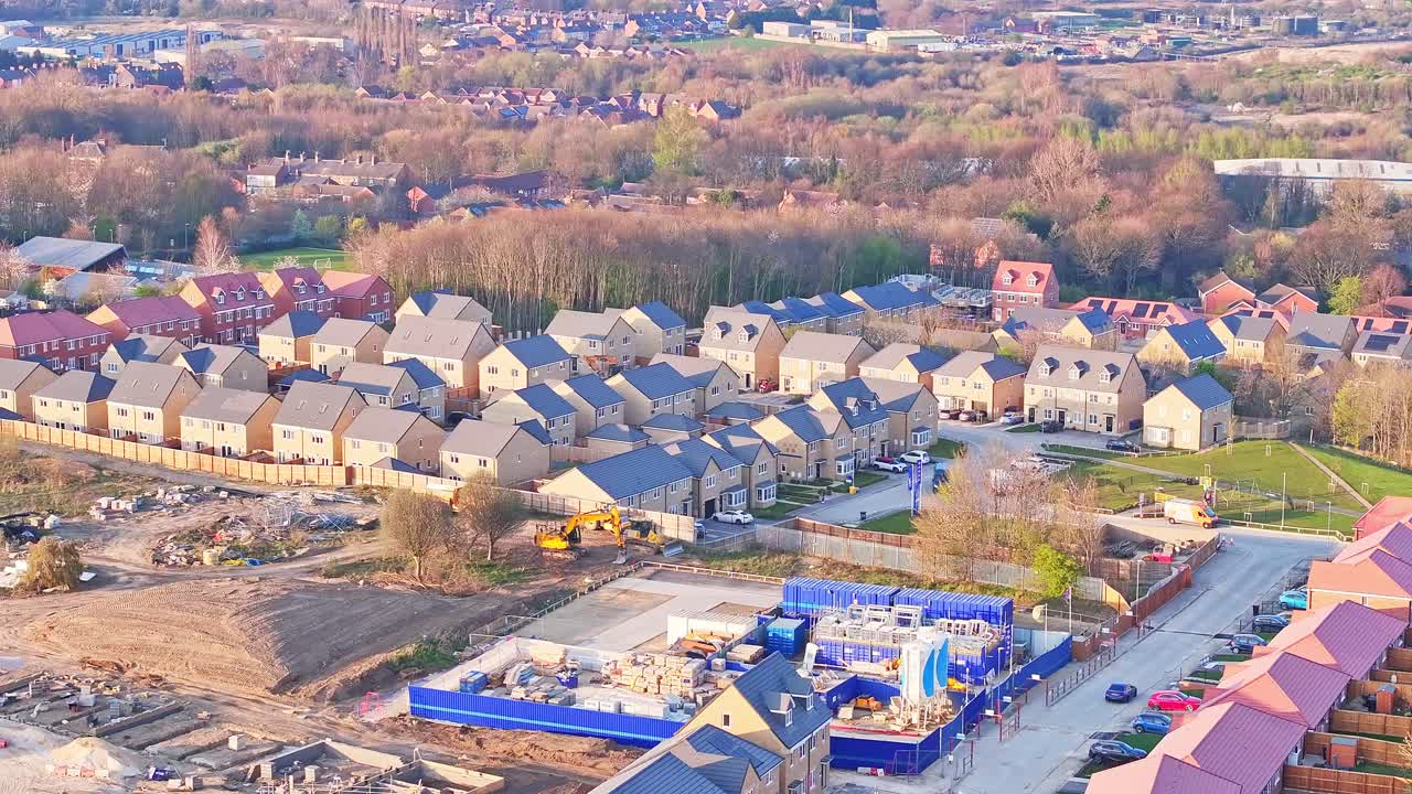 Sweeping aerial drone glide revealing new residential houses, active construction, green spaces, and surrounding woodland in Wombwell, South Yorkshire, England