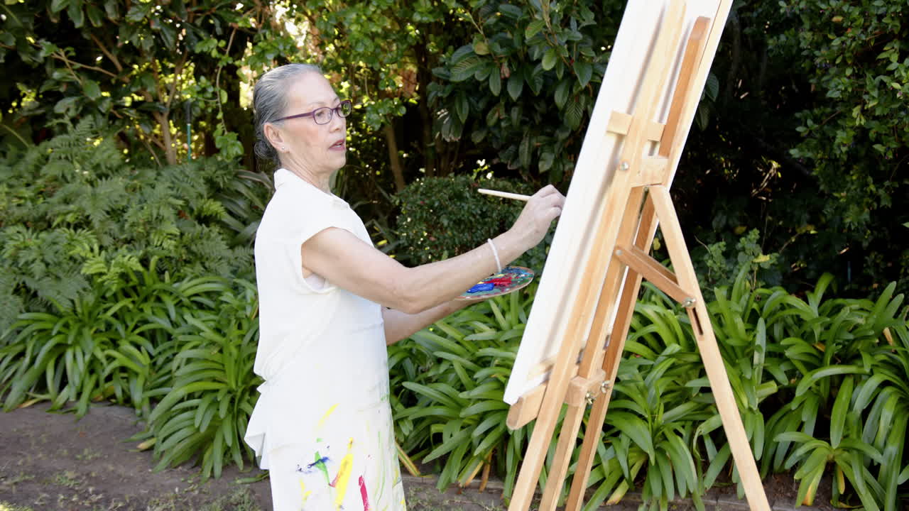 Painting on canvas, woman using paintbrush and palette in outdoor garden