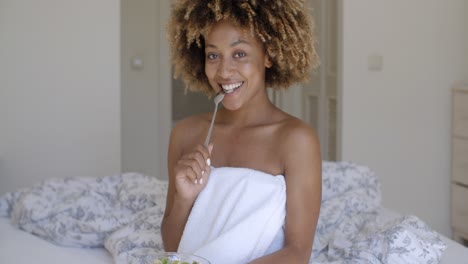 mujer joven en la cama comiendo ensalada de verduras