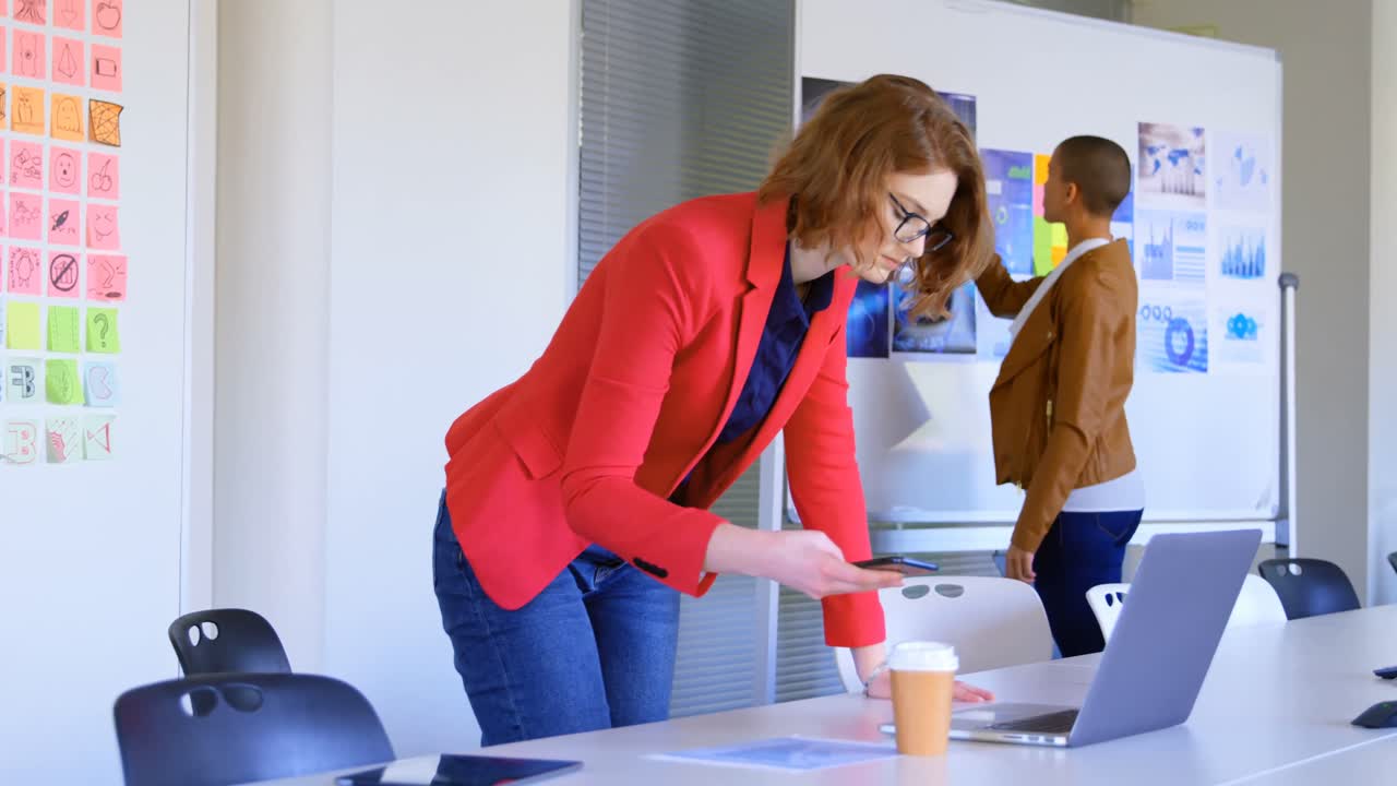 vista lateral de una joven ejecutiva caucásica usando un teléfono móvil mientras trabaja en una computadora portátil en el moderno