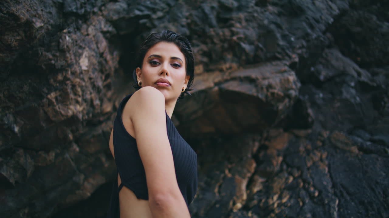 Confident brunette posing rocks at seashore closeup. Fashion model look camera