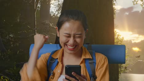 Close Up Of Asian Female Hiker With Mountaineering Backpack Looking At The Smartphone And Screaming Goal Celebrating The Success While Exploring Forest Nature