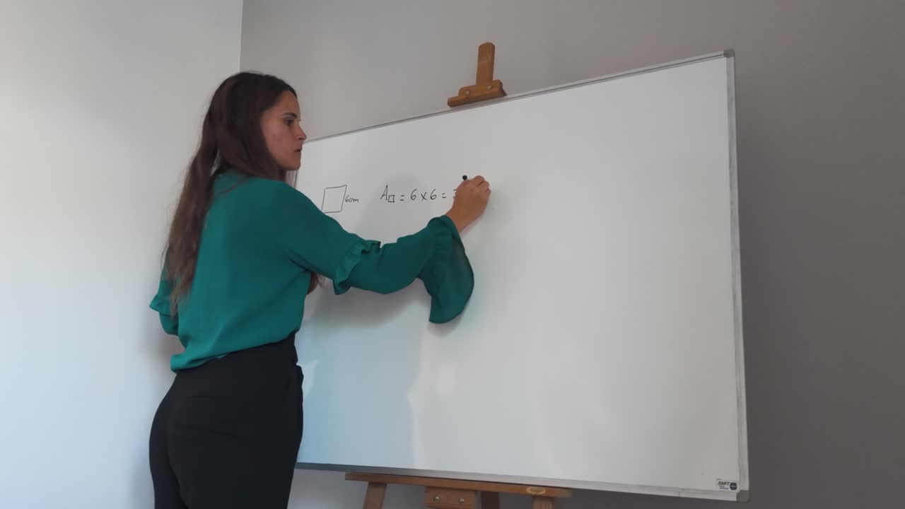 niña enseñando matemáticas en una pizarra en el interior, vestida profesionalmente escribiendo ecuaciones para el área del cuadrado