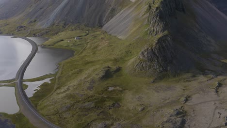 aerial tilt up shot of car driving on road along coast and mystic covered eystrahorn mountain in iceland