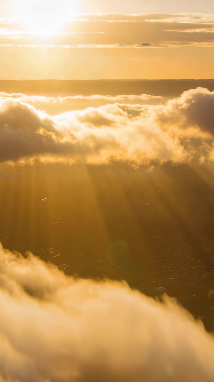 Vertical video: Nearing sun at golden hour causing sunlit cloud deck glowing and rays growing